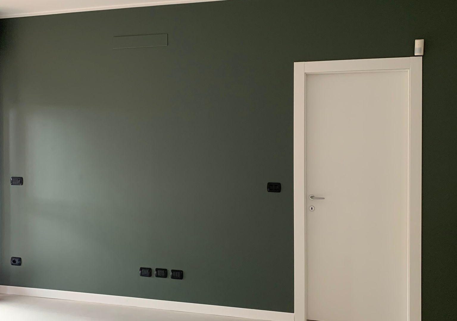 Parete di un soggiorno dipinta di verde scuro, con porta e battiscopa bianchi: un lavoro di Universal Color