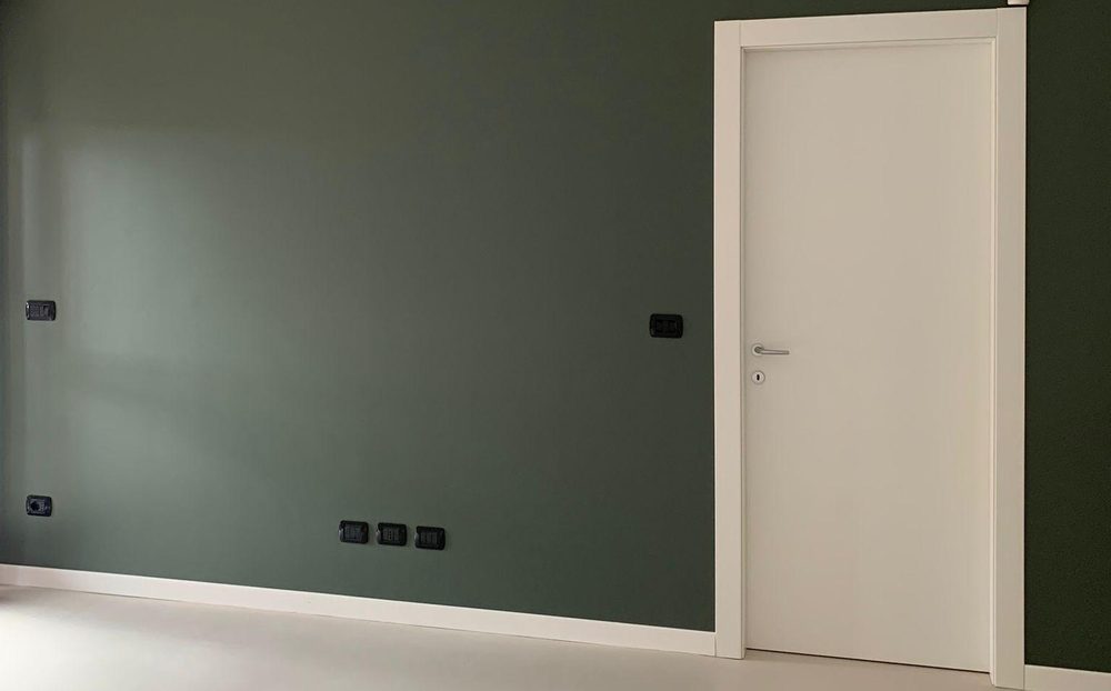 Soggiorno con parete verde scuro, porta e battiscopa bianchi appena dipinti